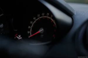 A close-up of a car's speedometer, with the needle resting at zero and dashboard details softly fading into shadow.